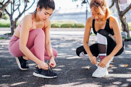 Young Asian female runners in park tying shoe lace. Women getting ready for a morning run in outdoor park for a healthy livingの写真素材