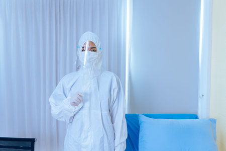 Portrait of young female Asian doctor wearing protective PPE suit with face shield and mask holding...