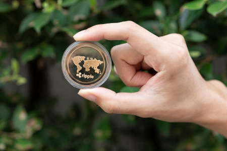 Young man holding XRP Ripple coin in hand with green bush in background - Cryptocurrency and Digital asset conceptの写真素材