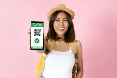 Happy young female traveler using mobile phone app showing travel pass of vaccination over pink isolated background.の写真素材