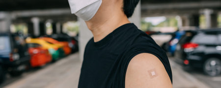 Young vaccinated man showing arms with adhesive plaster bandage after receiving Covid-19 vaccine...