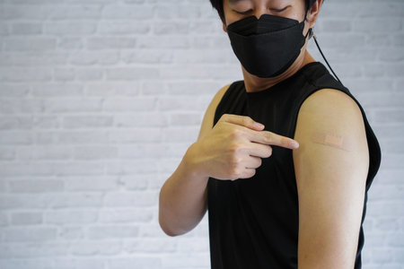 Young vaccinated man showing arms with adhesive plaster bandage after receiving Covid-19 vaccine...