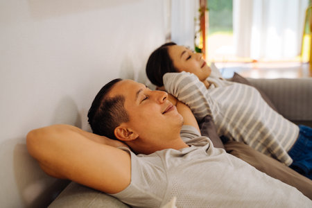 Side view of a couple relaxing on a sofa in living room at home. Caucasian and Asian woman breathing and resting while smiling and lying in couch indoorsの写真素材