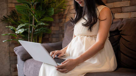 Top view of young beautiful Asian working pregnant woman using computer laptop and sitting on sofa at home - maternity leave from office work conceptの写真素材