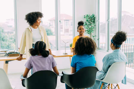Young adolescent African American boy talking in front of classroom while female teacher and classmates looking at him. School and education in Africa conceptの写真素材