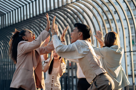 Group of excited Asian entrepreneurs giving high five to each other and celebrating success at party