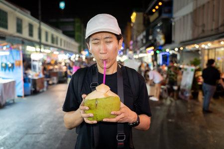 Portrait face of thirsty Asian solo hipster traveller holding a coconut drink on street in Bangkok, Thailand. Male tourist drinking a cococonut juice for refreshment. - copy spaceの写真素材