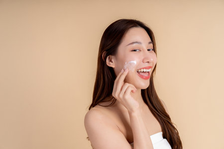 Closeup portrait of a face of the young Asian girl with a healthy facial skin rubbing her face with facial white cream in studio background. Skin care and dermatology concept.の写真素材