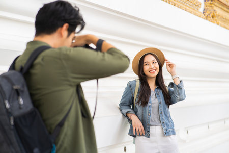 Portrait of Asian man and woman couple travelers in relationship. Boyfriend taking a photo of girlfriend in temple on street in Bangkok, Thailand, Southeast Asia - people traveling photography conceptの写真素材