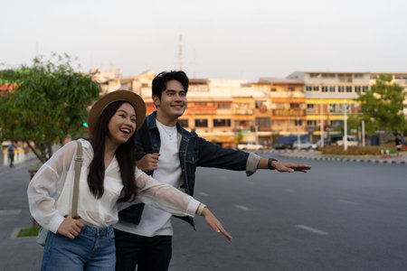 Happy smiling Young Asian couple traveler tourists hailing for taxi cab on the street in Bangkok in Thailand with no phone or use of technologyの写真素材