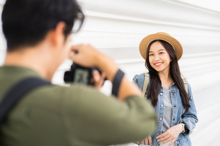 Portrait of Asian man and woman couple travelers in relationship. Boyfriend taking photo of girlfriend in front of buddhist temple on street in Bangkok, Thailand - people traveling photography conceptの写真素材