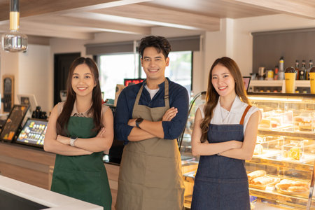 Asian barista male and female colleagues standing with arm crossed and looking at camera and smiling at cafe shop. Happy working a small business togetherの写真素材