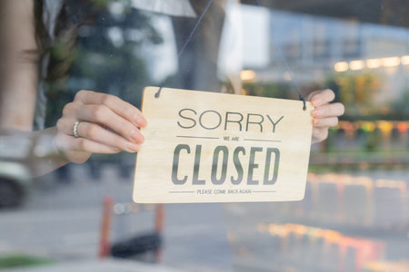 Female store owner turning close sign board of start up coffee shop cafe and restaurant through the...