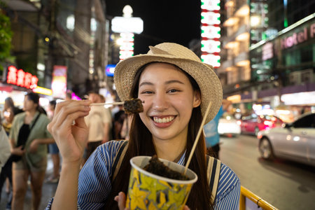 Happy young adult asian foodie woman backpack traveller eating asia street food. People traveling to China town street market. Bangkok, Thailandの写真素材