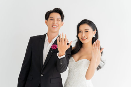 Love and commitment reflected in the smiles of an Asian couple as they present their wedding ring. Joyful Asian bride and groom share a moment of bliss, showcasing a sparkling wedding ring.の写真素材