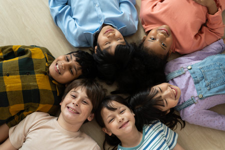 Diverse group of happy children lying on the floor in a circle, smiling and bonding together,...