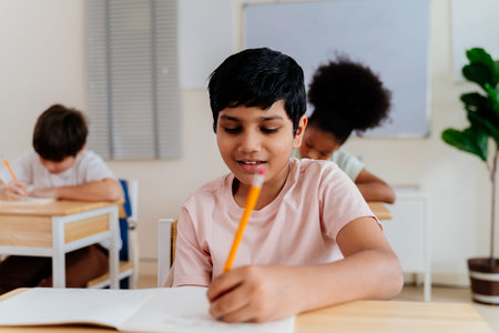 Happy Indian boy in a classroom setting, smiling brightly while writing. Young student with afro...