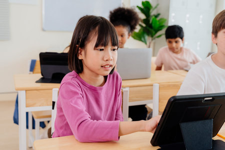 Young Asian girl engages with tablet in diverse elementary classroom. Students embrace digital...