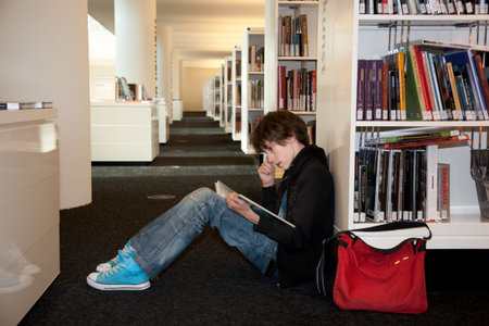 teenager reading a book in a library in front of a window overviewing the city  expressing building...