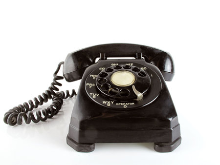Old-fashioned balck telephone sits on a white reflective surface                               