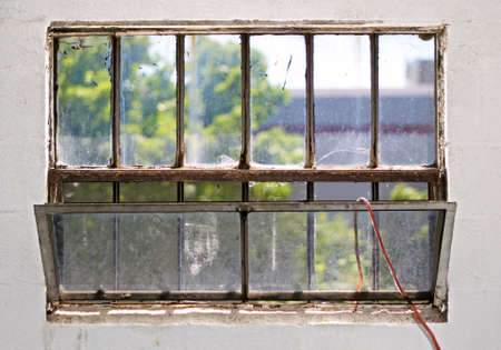 Grungy, dirty, rust basement casement window with an old red garden hoseの写真素材
