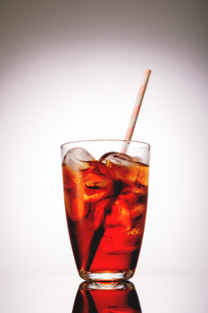 Cola in glass with ice on grey background.
