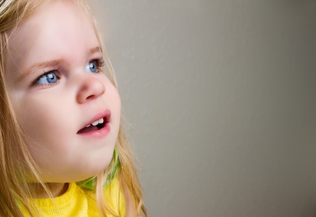 Portrait of cute baby girl or toddler with blond hair and blue eyes. Gray background and copy space.の写真素材