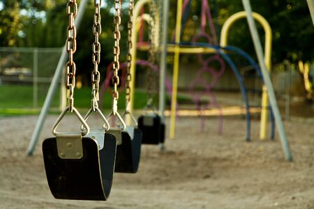 Swing set at a playground that is empty. Lighting is warm due to the being taken at sunsetの写真素材
