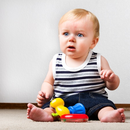 Young toddler sitting up on the floor with a ring and a toy hammer to play with.の写真素材