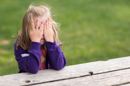 Preschooler playing game of hide and sick. Right now she is sitting on the table covering her eyes while taking a sneaky peek.の写真素材