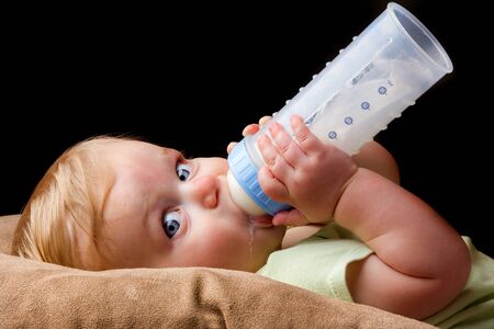 A little guy is drinking from his milk bottle very heavily. Even has a little milk drool coming out.の写真素材