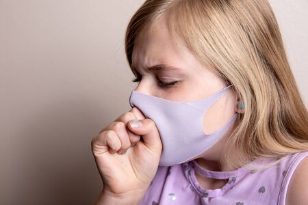 Sick young girl coughing into her maskの写真素材