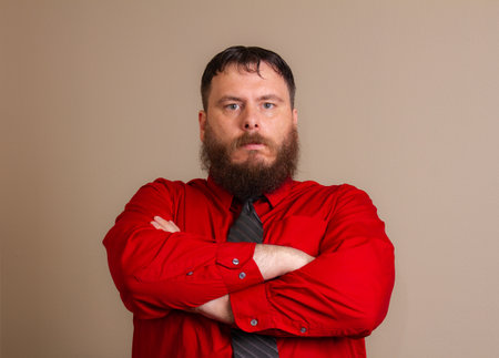 A man with a beard and a red shirt is standing with his arms crossedの写真素材