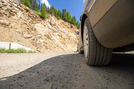 A car is parked on a dirt road next to a rocky hill