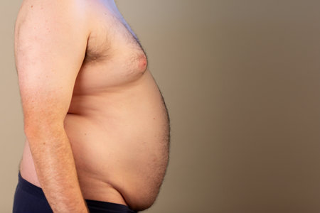 A man with a large belly is standing in front of a wallの写真素材