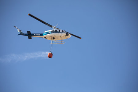 October 4, 2024 - Boise, Idaho: A helicopter is flying in the sky with a red water bucket attached...
