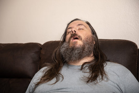 A man with a beard and long hair is sleeping on a couchの写真素材