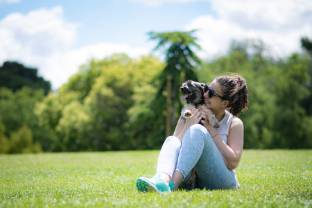 young woman playing affectionately with small dog of the yorkshire breed in garden with grass and...