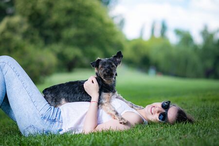 young woman playing affectionately with small dog of the yorkshire breed in garden with grass and trees.の写真素材
