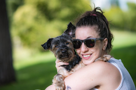 young woman playing affectionately with small dog of the yorkshire breed in garden with grass and trees.の写真素材