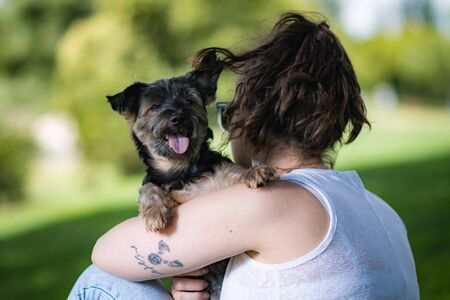 young woman playing affectionately with small dog of the yorkshire breed in garden with grass and trees.の写真素材