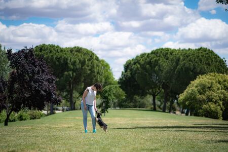 young woman playing affectionately with small dog of the yorkshire breed in garden with grass and trees.の写真素材