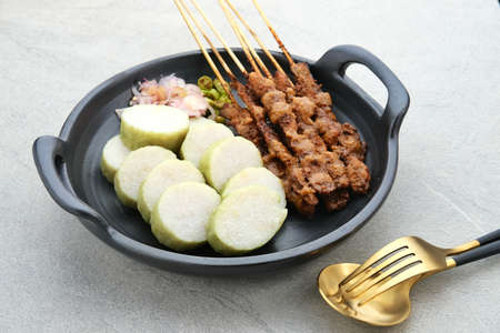 Sate Ayam (Chicken satay) with peanut sauce and lontong (rice cake). One of the popular street food in Indonesia. Served in black plate on the table.の写真素材