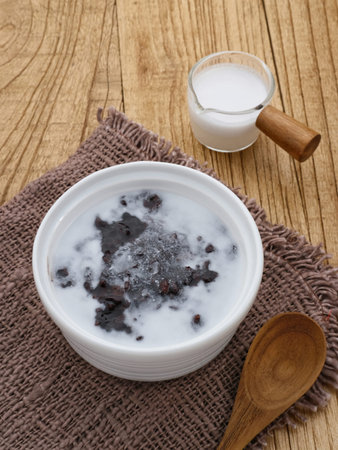 Bubur Ketan Hitam, Indonesian dessert. Black glutinous rice porridge with coconut milk, sugar and pandan leaf. Served in a white bowl on a wooden table. Blurred background and selective focus.の写真素材