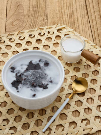 Bubur Ketan Hitam, Indonesian dessert. Black glutinous rice porridge with coconut milk, sugar and pandan leaf. Served in a white bowl on a wooden table. Blurred background and selective focus.の写真素材