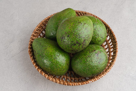 Alpukat or Avocado (Persea americana), ripe and fresh, served in rattan basket on grey background,...
