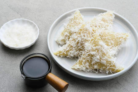Lupis or Lopis, a traditional Indonesian food made from sticky rice and wrapped in banana leaves. Served with grated coconut and liquid brown sugar. Selective focus image.の写真素材