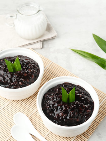 Bubur Ketan Hitam, Indonesian dessert. Black glutinous rice porridge with coconut milk, sugar and pandan leaf. Served in a white bowl. Blurred background and selective focus.の写真素材