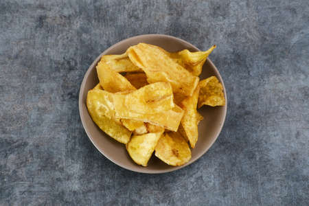 Heap of dried banana chips snack in small bowl on dark background. Selective focus image, blurred background.の写真素材