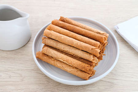 Waffle egg rolls or semprong cake, a traditional Indonesian snack with a unique shape like a layered pipe, served on a white plate. Selected focus.の写真素材